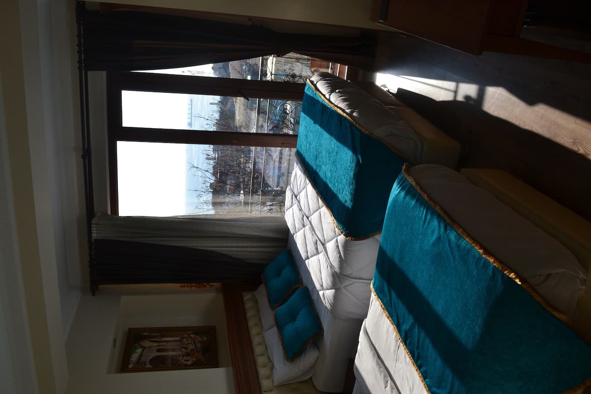 A room with a large window, a bed with blue and white bedding, and a framed picture on the wall.