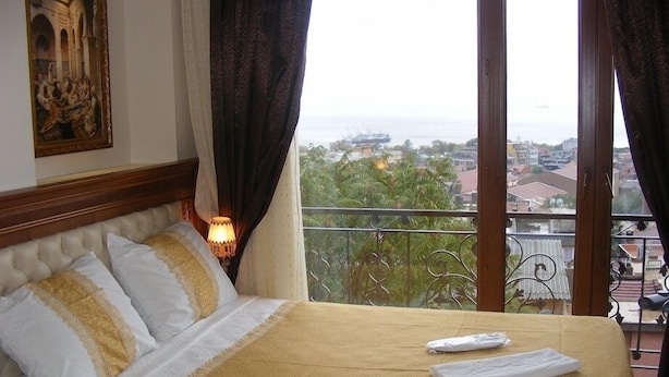 A hotel room with a bed, a painting on the wall, a balcony with a view of the city and sea, and a window with curtains. - Hotel Blue Istanbul - Special class (Istanbul)
