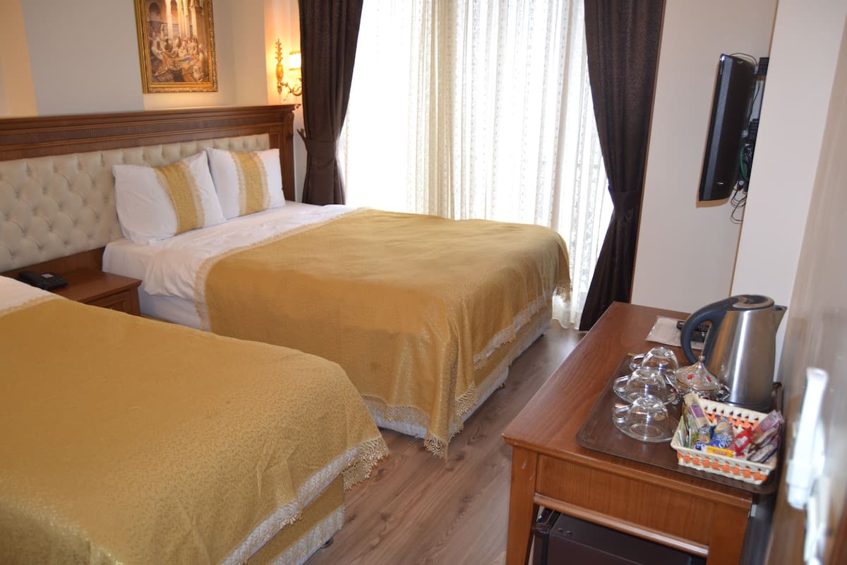 A hotel room with two beds, a wooden headboard, a small table with a kettle, glasses, and a tray of items.