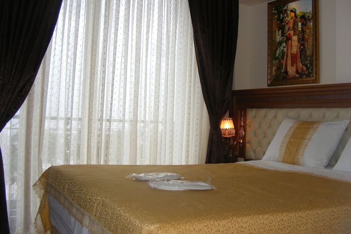 A hotel room with a bed, curtains, a painting, and a lamp.