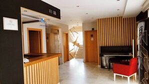 Hotellin aula, jossa on vastaanottotiski, portaikko, joka johtaa ylempään kerrokseen, piano ja punainen tuoli.