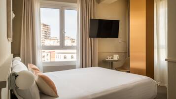 Une chambre d’hôtel avec un lit, des rideaux, une télévision, une petite table avec une machine à café et une vue sur les bâtiments à l’extérieur de la fenêtre.
