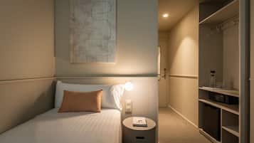 Ein Hotelzimmer mit einem ordentlich bezogenen Bett, einem Nachttisch mit Lampe, einem an der Wand hängenden abstrakten Kunstwerk und einem begehbaren Kleiderschrank mit Regalen.