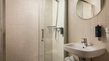 Un baño moderno con cabina de ducha de vidrio, un lavabo blanco y un espejo redondo.