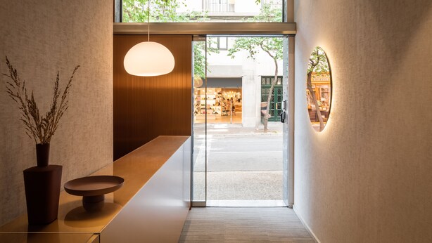 Un interior moderno con un banco de madera, un florero con plantas secas y una puerta de vidrio que da al exterior.