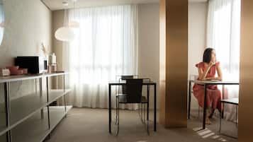 A modern hotel room with a desk, chair, and a large window with sheer curtains.