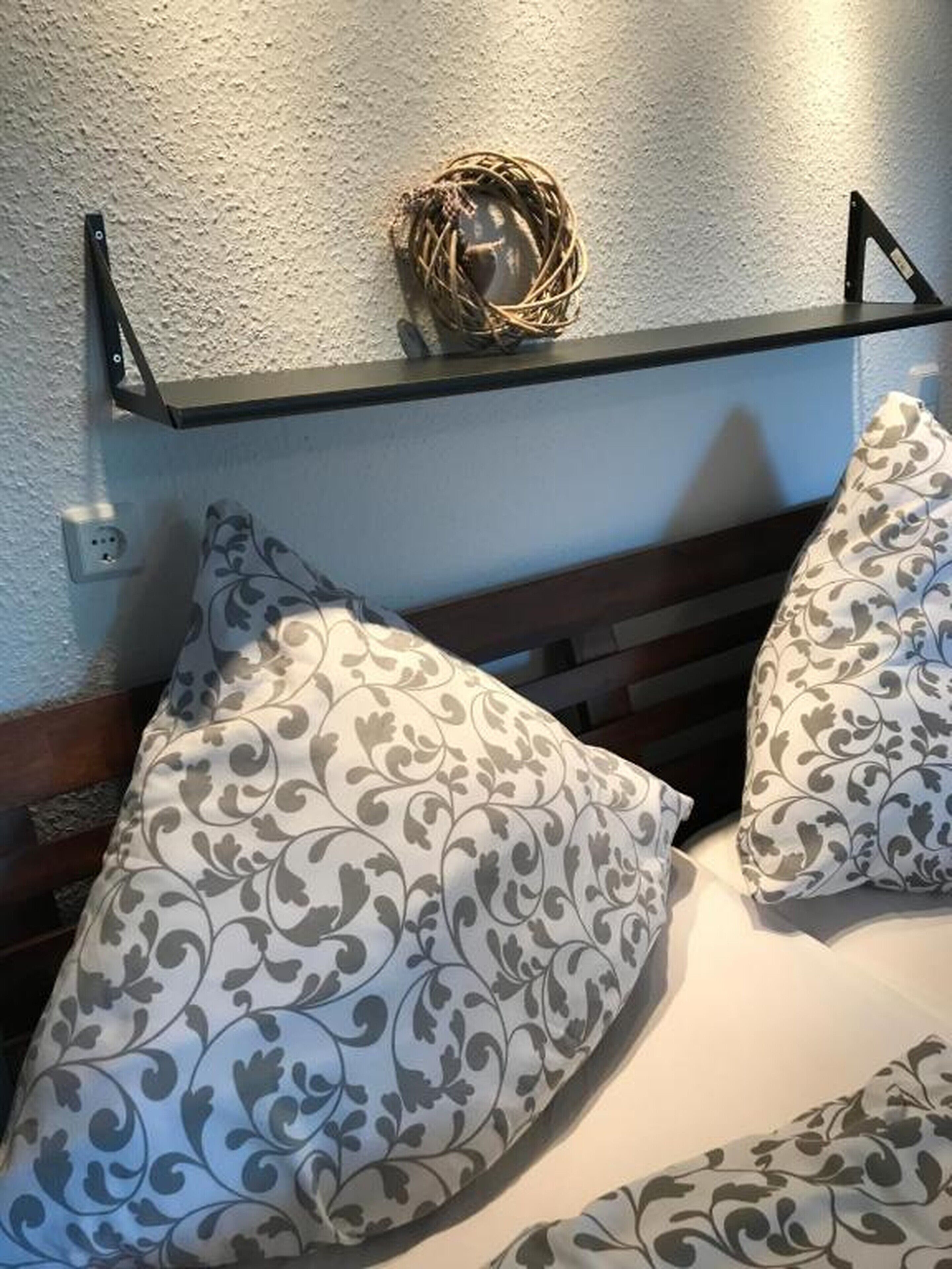 A bed with patterned pillows and a woven basket on a shelf above.