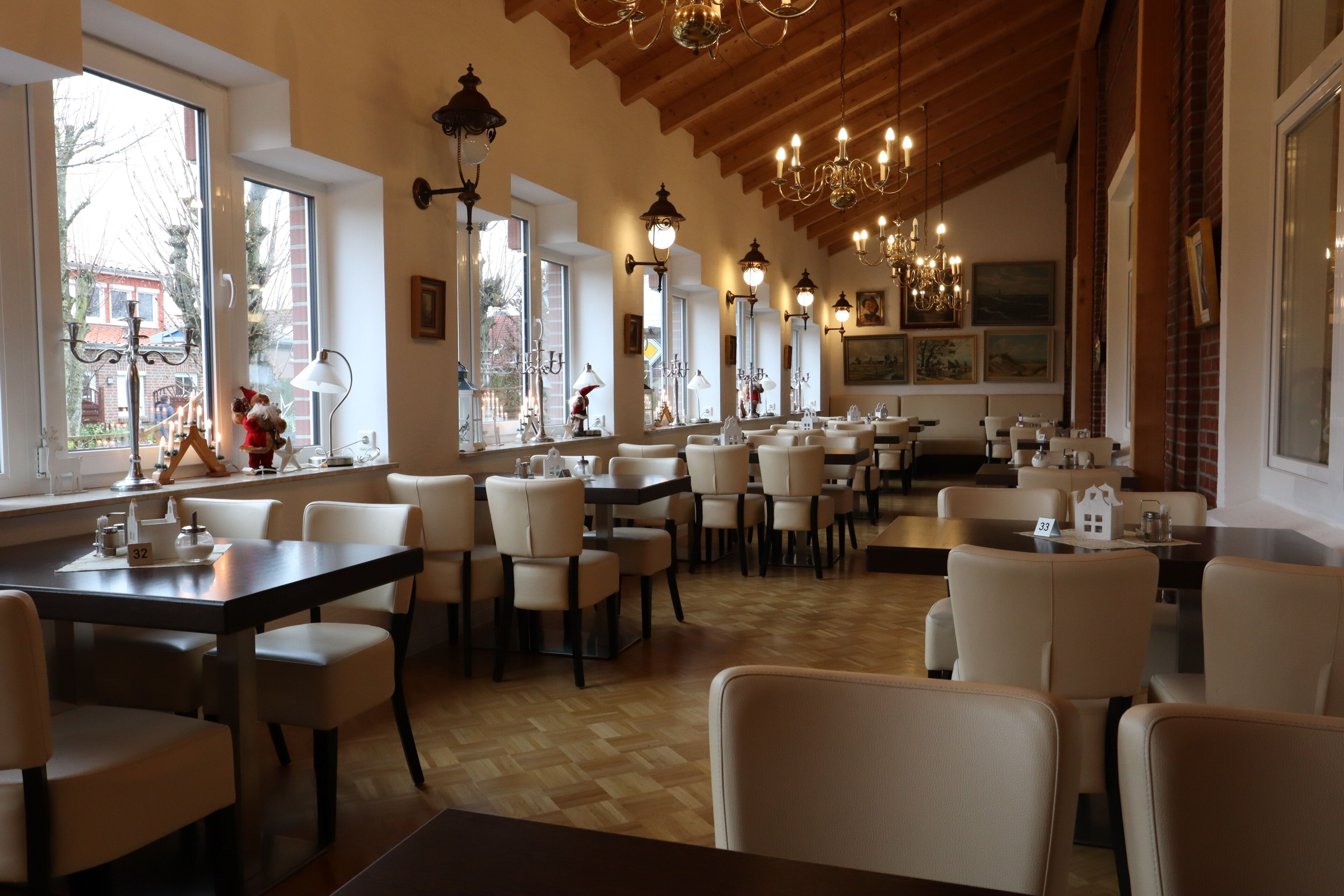 Un restaurante con varias mesas y sillas, ventanas amplias y lámparas de araña colgantes.