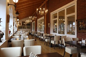 Un restaurant doté de nombreuses tables et chaises, de grandes fenêtres et de lustres suspendus.
