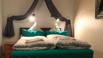 A bedroom with a canopy bed, green bedding, and a bedside table.