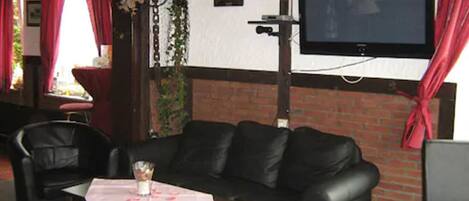 A cozy seating area with a sofa and chairs, a table with a glass, and a flat-screen TV mounted on the wall.