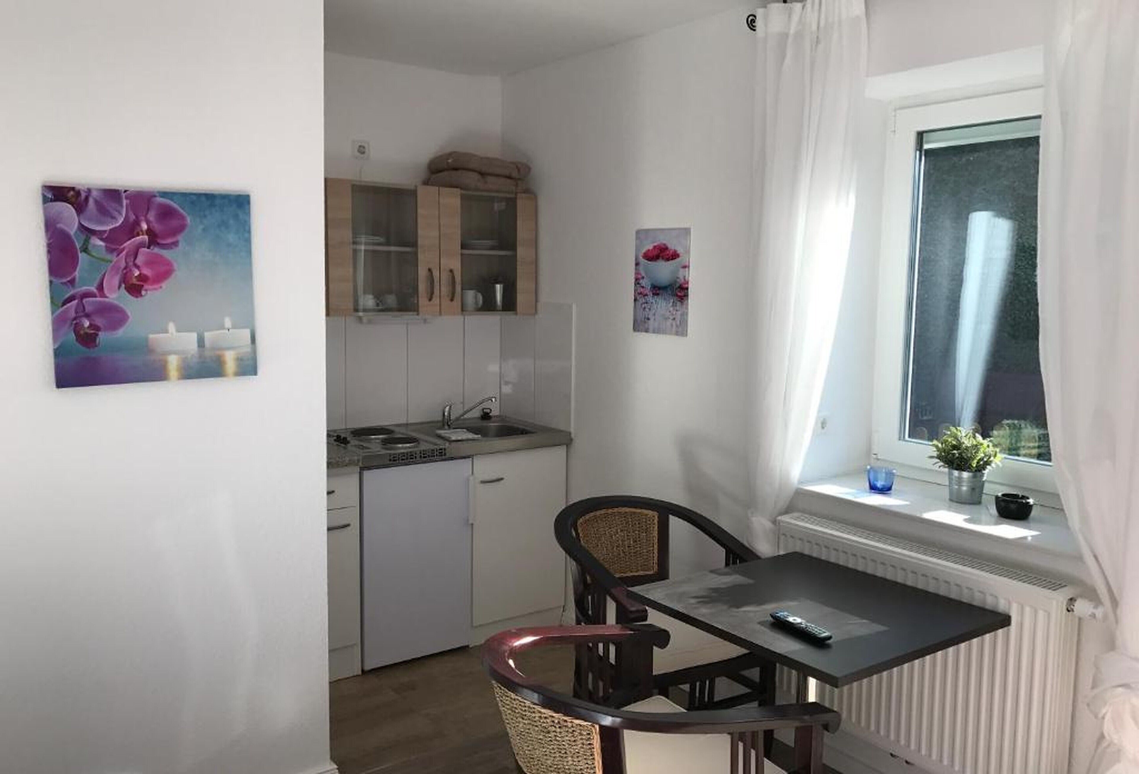 A compact kitchen with white cabinets, a dining table with two chairs, and a window with a view of the outdoors.