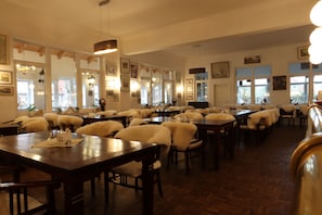 Un restaurante con varias mesas y sillas, suelo de madera y cuadros en las paredes.