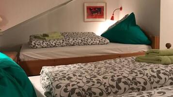 Un dormitorio con dos camas, una con cubrecama estampado y la otra con un diseño liso. Hay dos cuadros en la pared, una lámpara roja y un cojín verde en una de las camas.