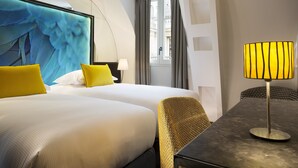 Habitación de hotel con dos camas, un escritorio, una lámpara y una obra de arte abstracta de gran tamaño en la pared.