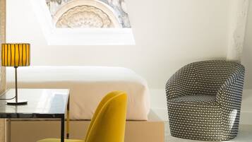 Una habitación de hotel moderna con una cama, un escritorio, una silla amarilla y un sillón estampado.