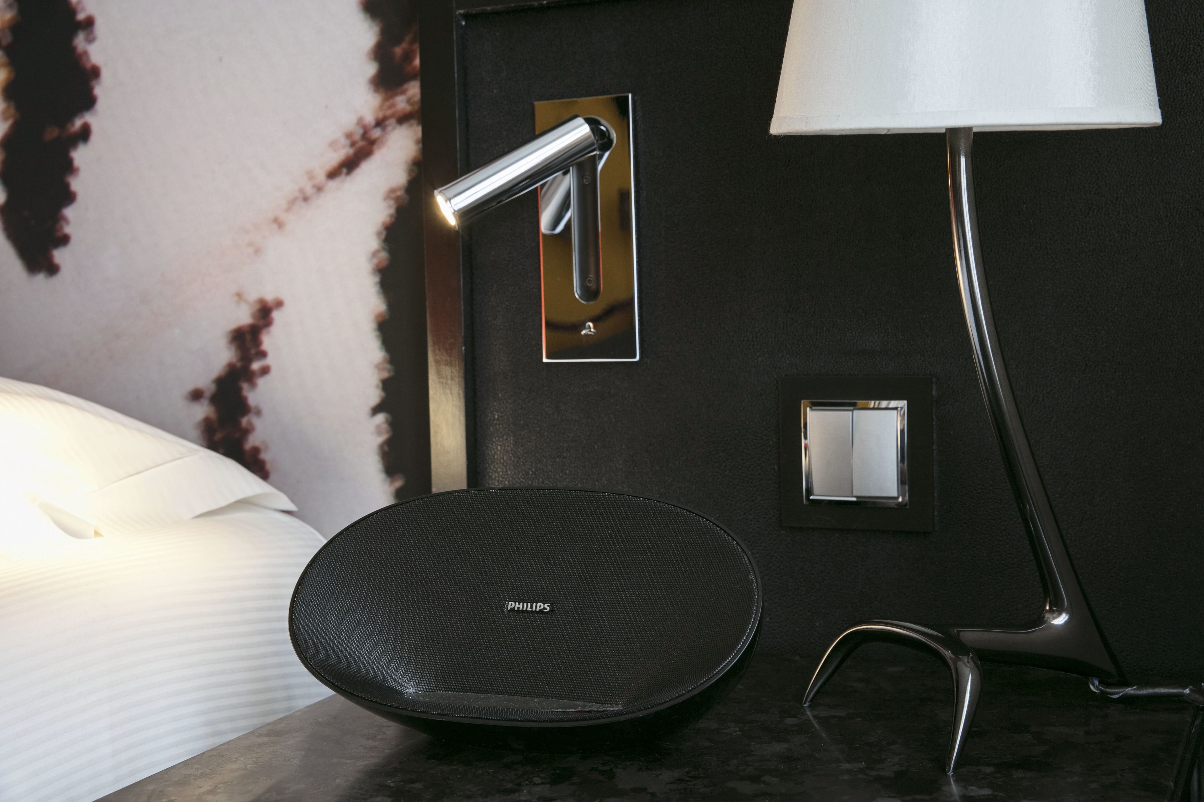 Een moderne badkamer met een zwarte wastafel, een spiegel, een wandlamp en een witte bedlamp.