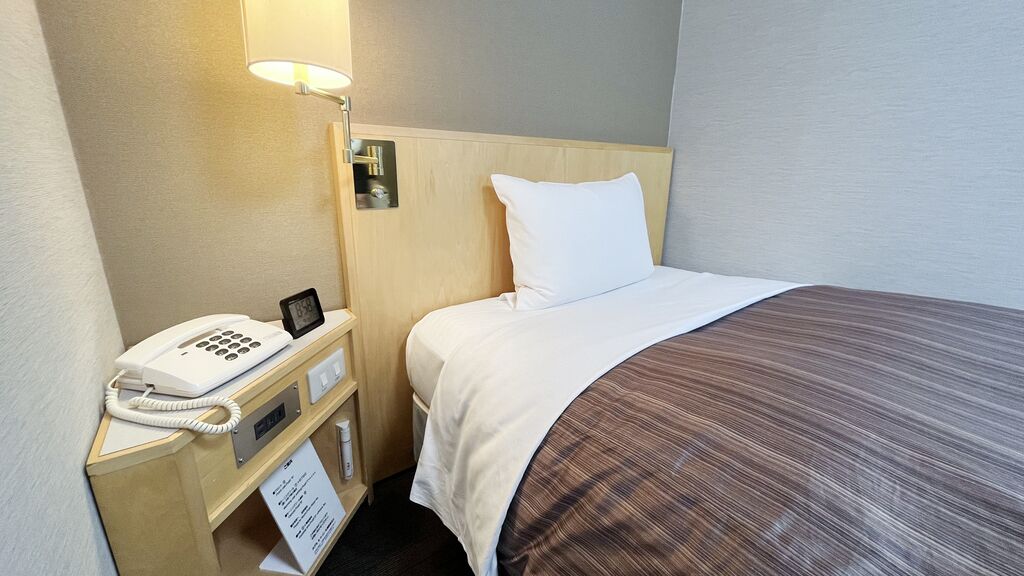 A hotel room with a bed, a bedside telephone, a lamp, and a sign with room information.