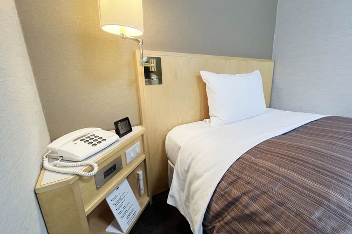 Une chambre d’hôtel équipée d’un lit, d’un téléphone sur la table de chevet, d’une lampe et d’un panneau indiquant les informations relatives à la chambre.