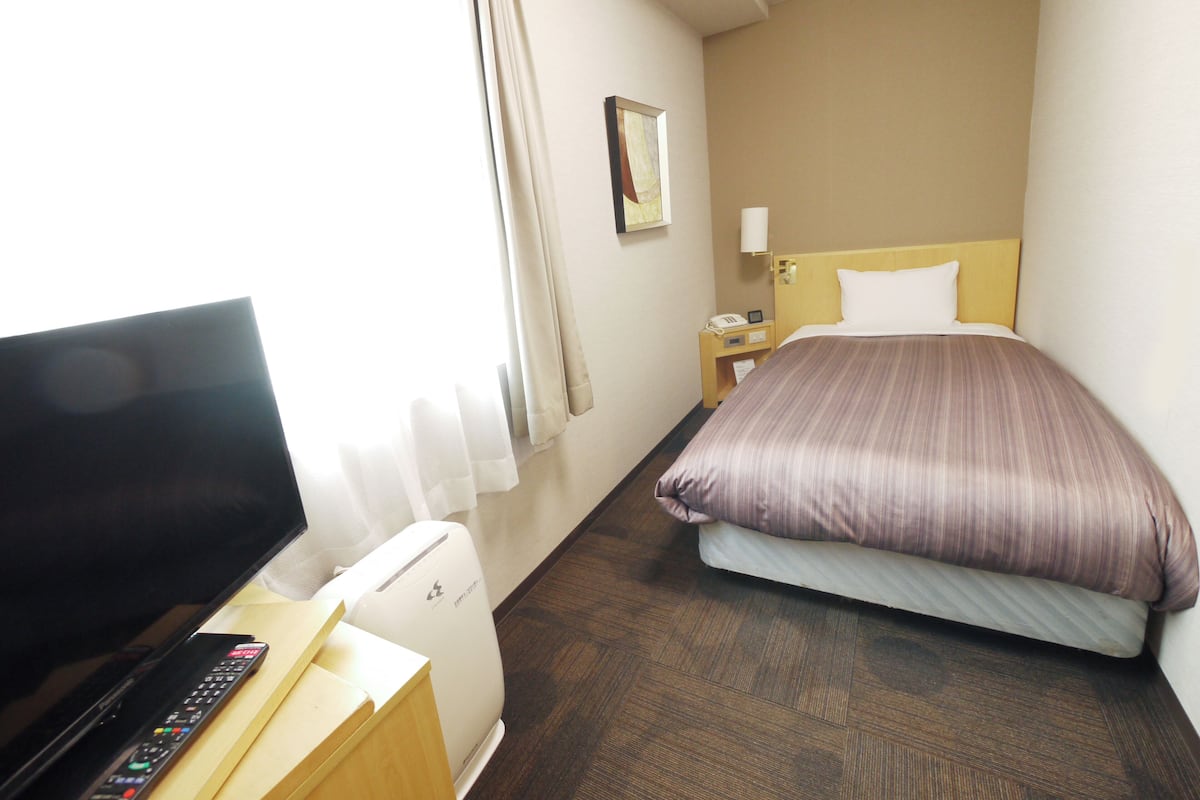 Une chambre d’hôtel équipée d’un lit, d’une télévision, d’une télécommande, d’une table de chevet et d’une lampe fixée au mur.