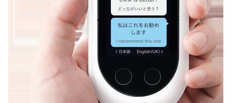 A hand holding a white pocket-sized device with a screen displaying text in English and Japanese.