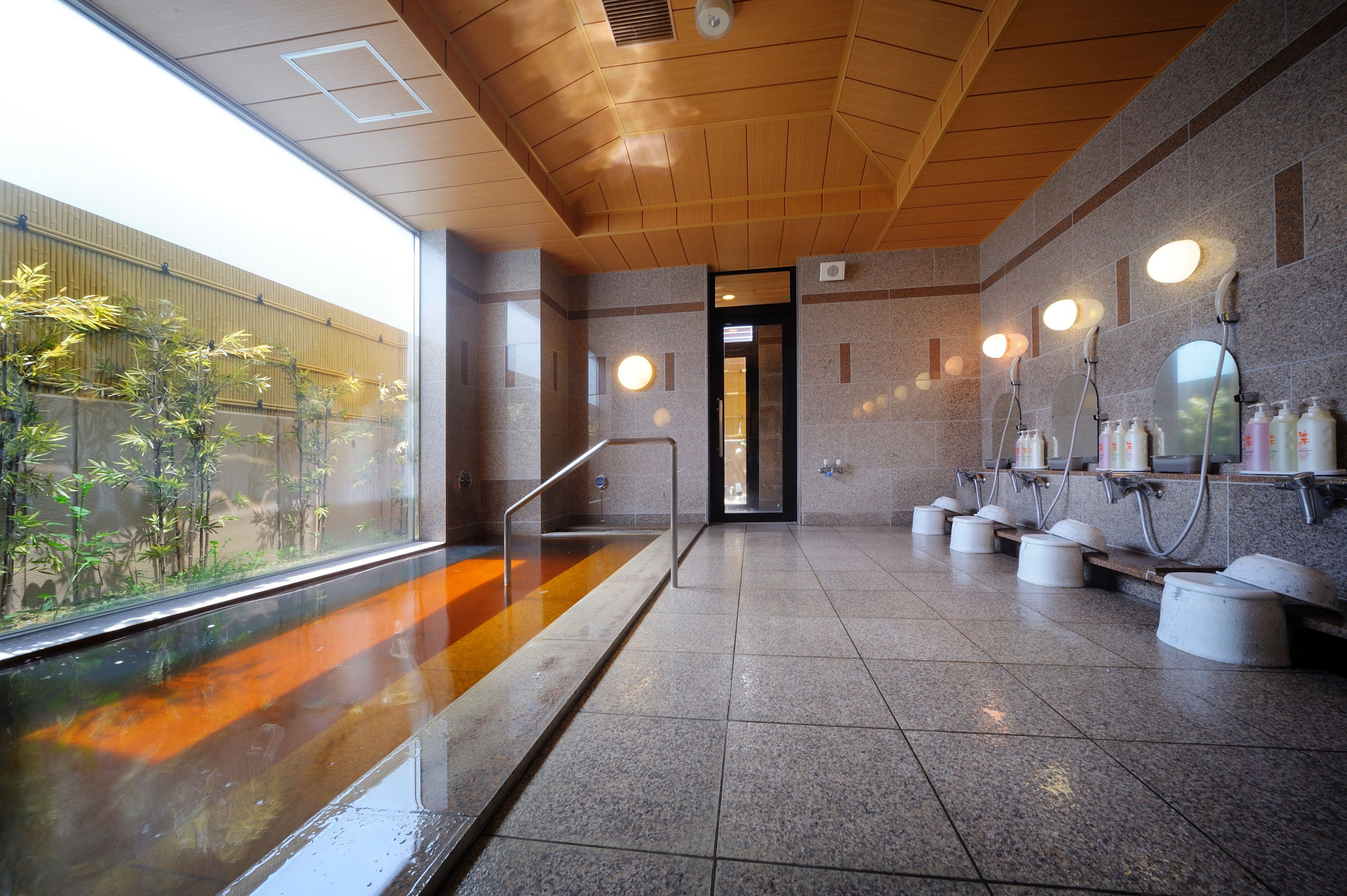 A public restroom with a glass enclosure, a wooden ceiling, and tiled floors.