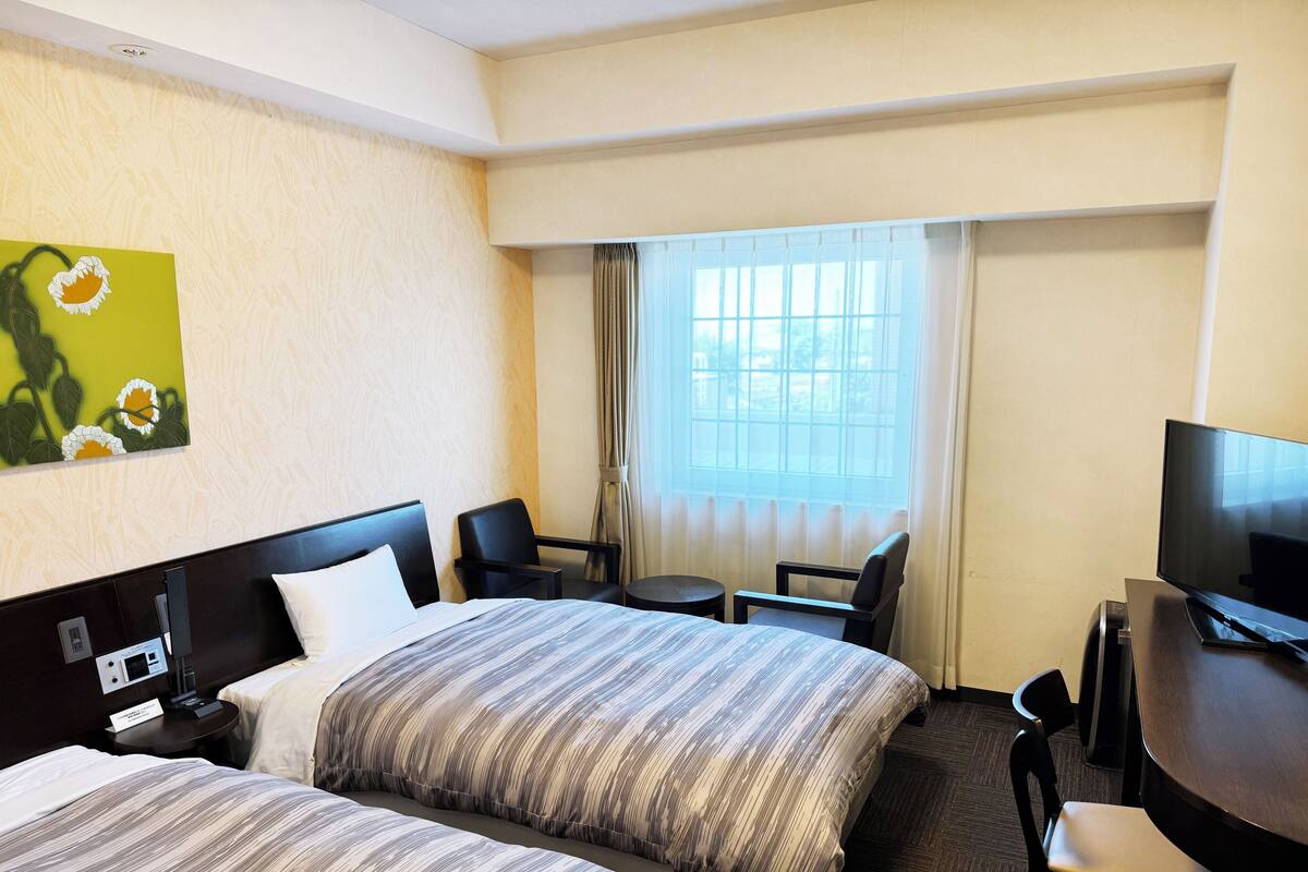 Een hotelkamer met twee bedden, een bureau met televisie, een klein tafeltje en een raam met gordijnen.