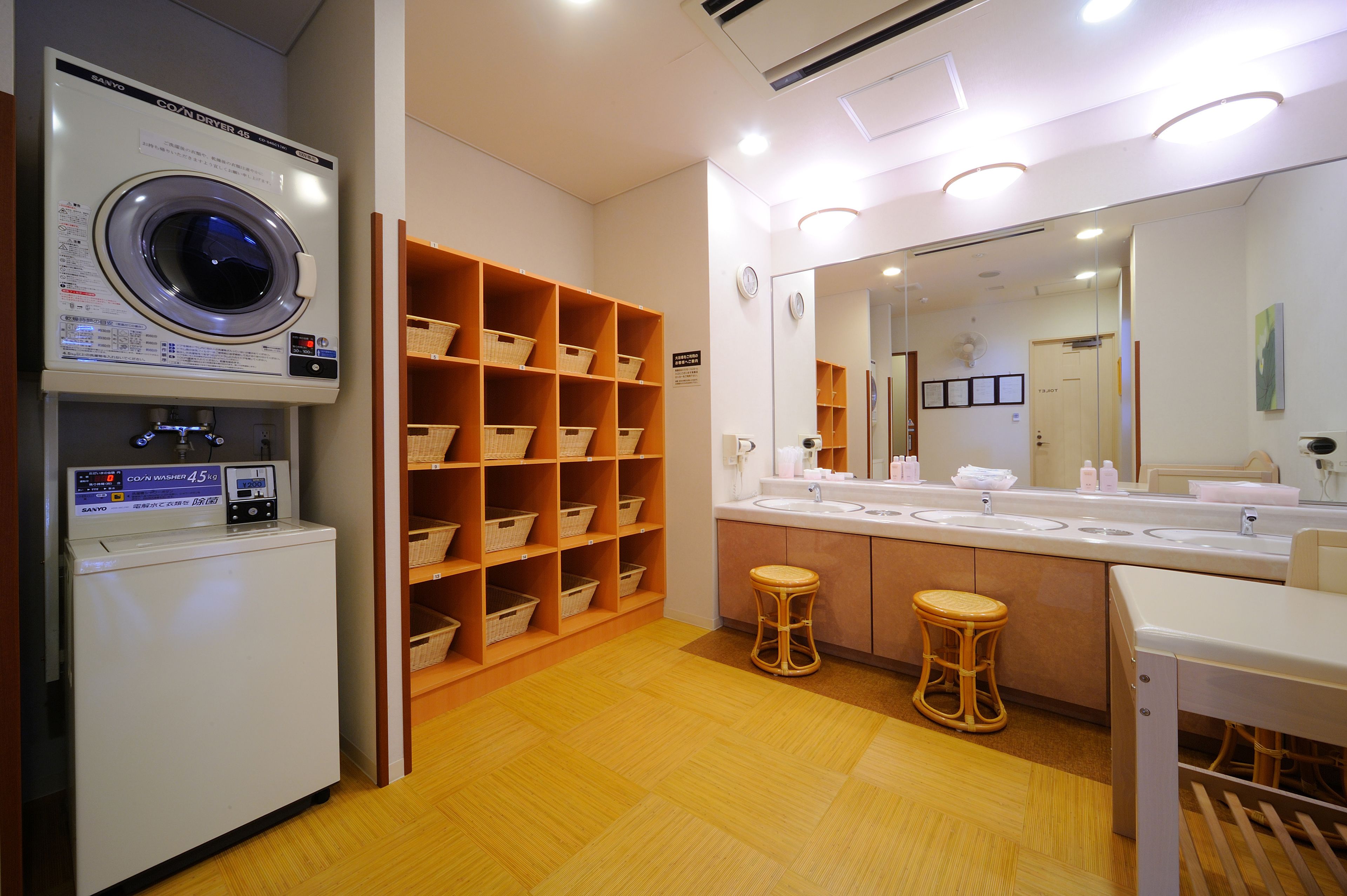 A hotel bathroom with a washing machine, shelves with baskets, a sink, and a mirror.