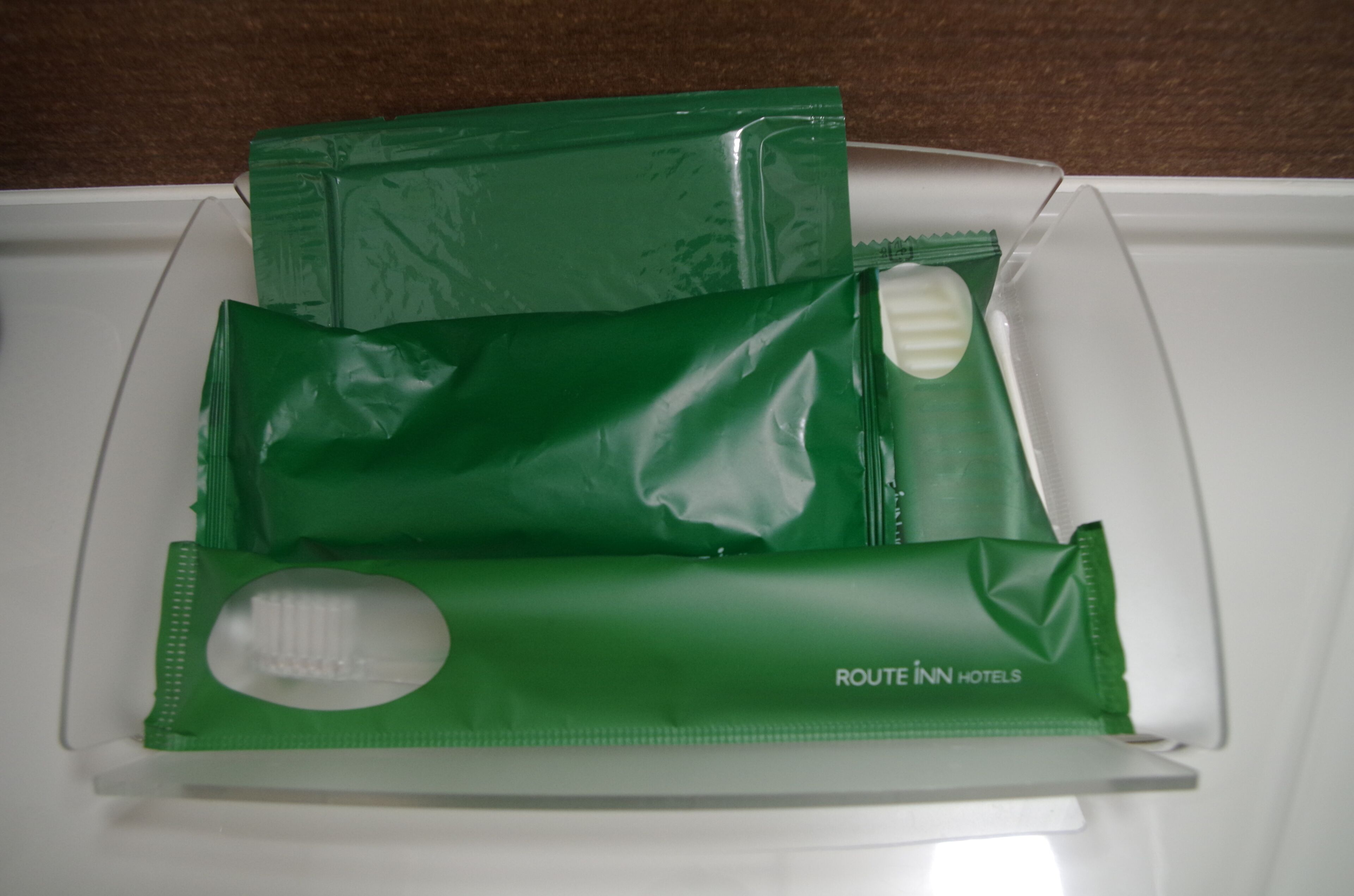 Bandeja blanca con artículos de aseo en verde, incluyendo un cepillo de dientes y una pastilla de jabón.