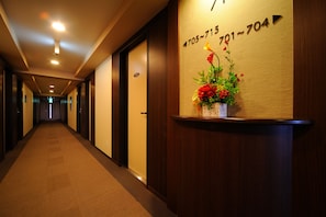A hotel hallway with a reception desk displaying phone numbers and a floral arrangement.