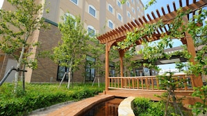 A wooden bridge over a small water feature, surrounded by greenery and a pergola structure. - Route-Inn Grantia Shiretoko Shariekimae (Shari)
