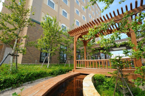 A wooden bridge over a small water feature, surrounded by greenery and a pergola structure.
