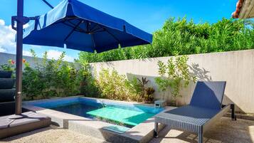 Une piscine avec un fauteuil de relaxation et un parasol.