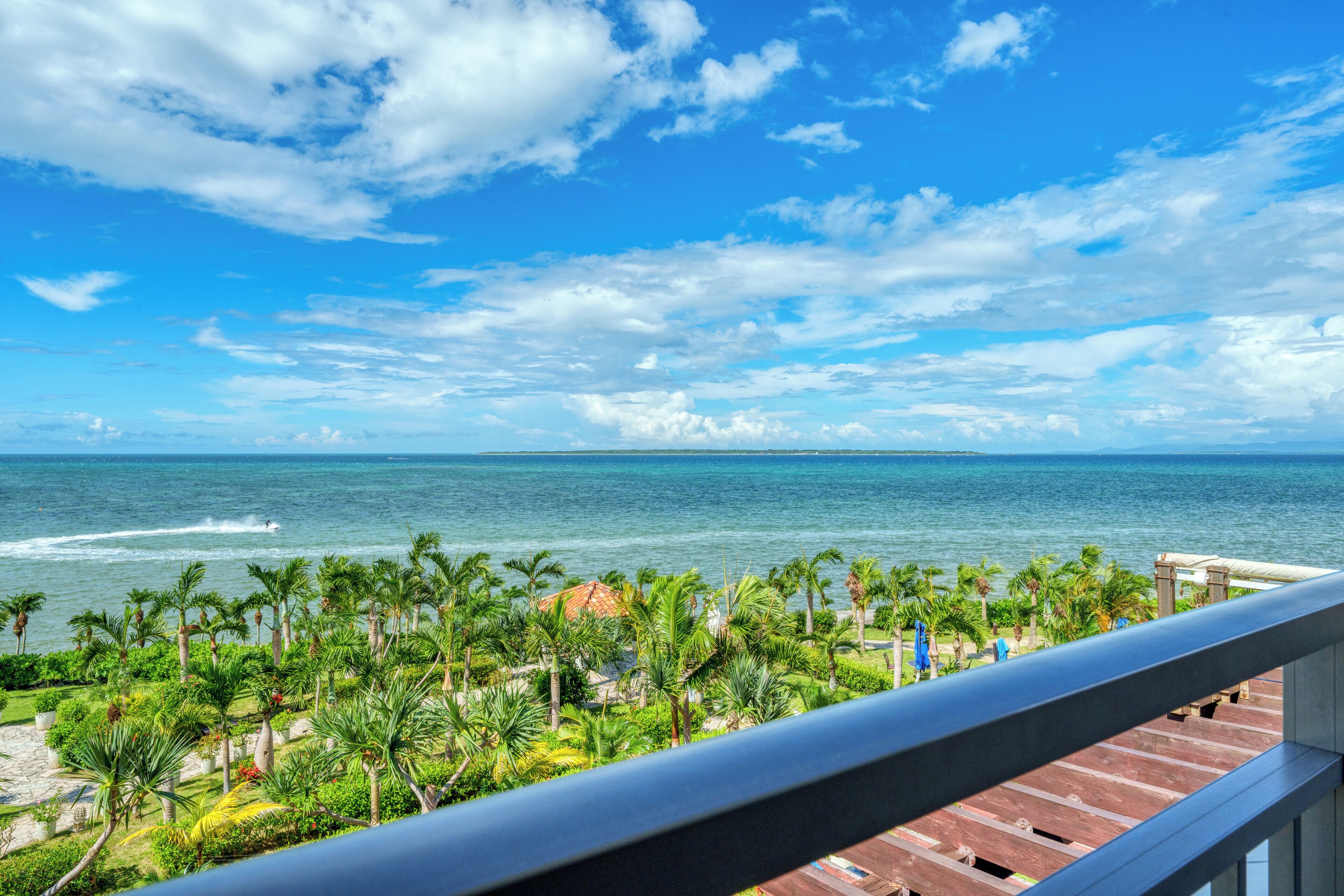 A balcony with a view of the ocean, palm trees, and a distant island.