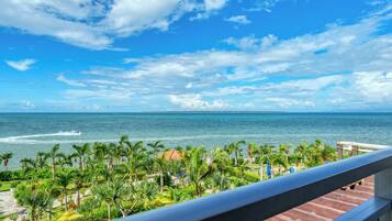 A balcony with a view of the ocean, palm trees, and a distant island.