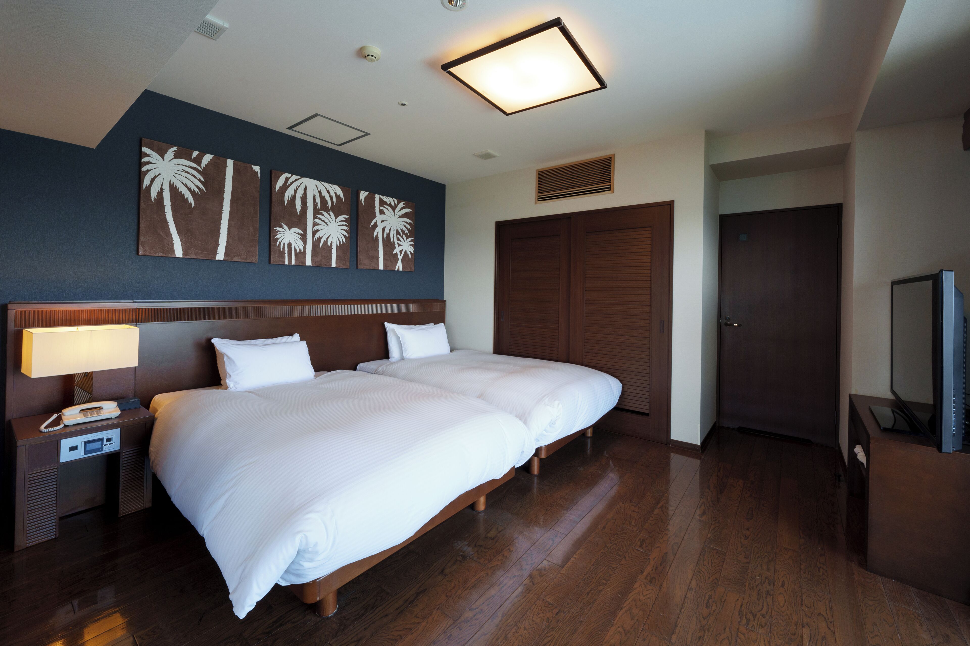 A hotel room with a large bed, a bedside table with a lamp, a TV, and artwork on the wall.