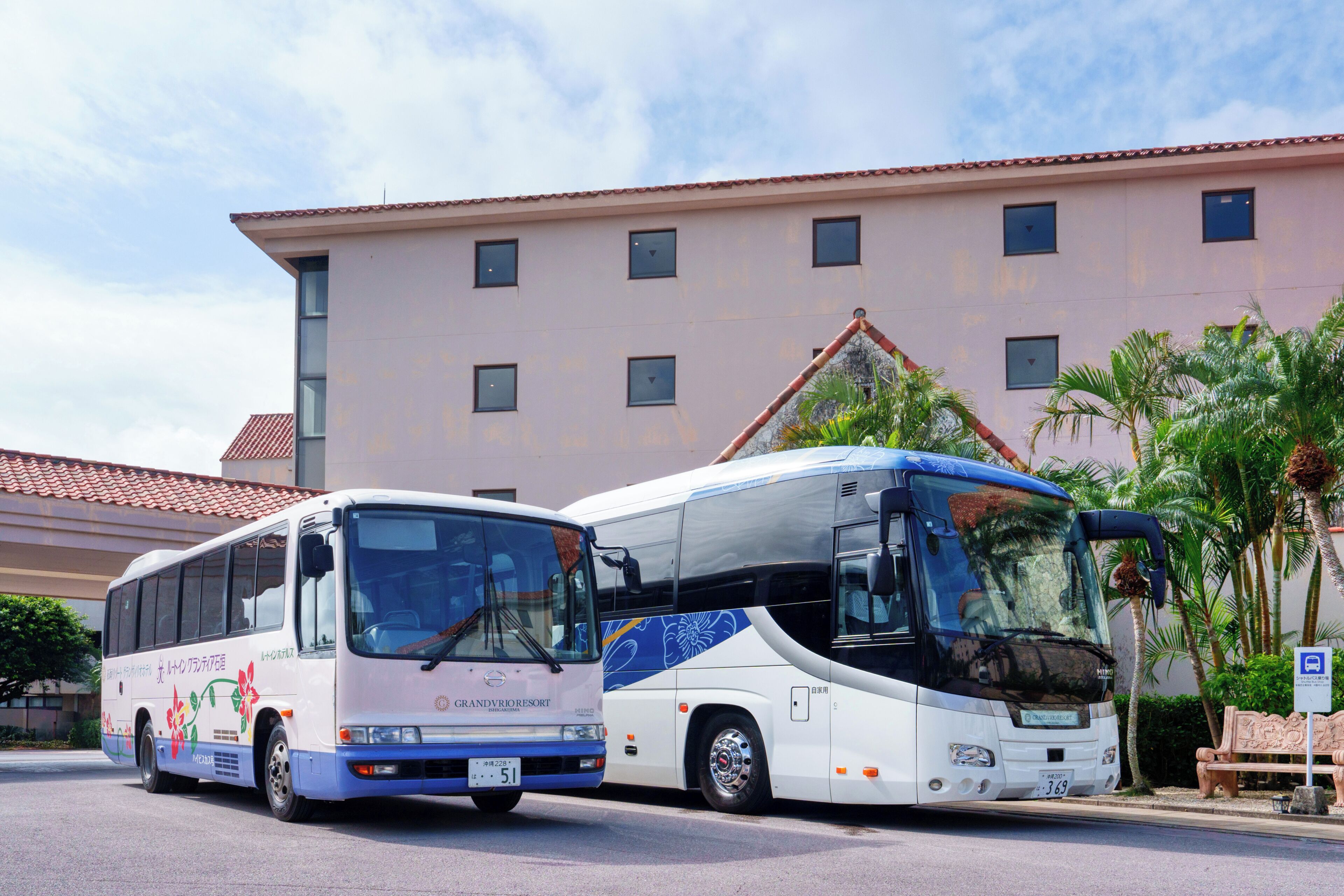 Dos autobuses estacionados frente a un edificio con techo de tejas y varias ventanas.