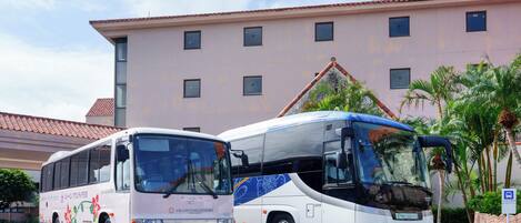 Dos autobuses estacionados frente a un edificio con techo de tejas y varias ventanas.