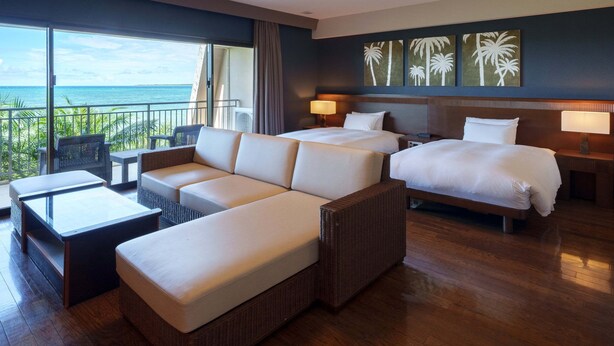 A hotel room with a large bed, a sofa, a small table, and a balcony with a view of the ocean. - Grandvrio Resort Ishigakijima (Ishigaki)