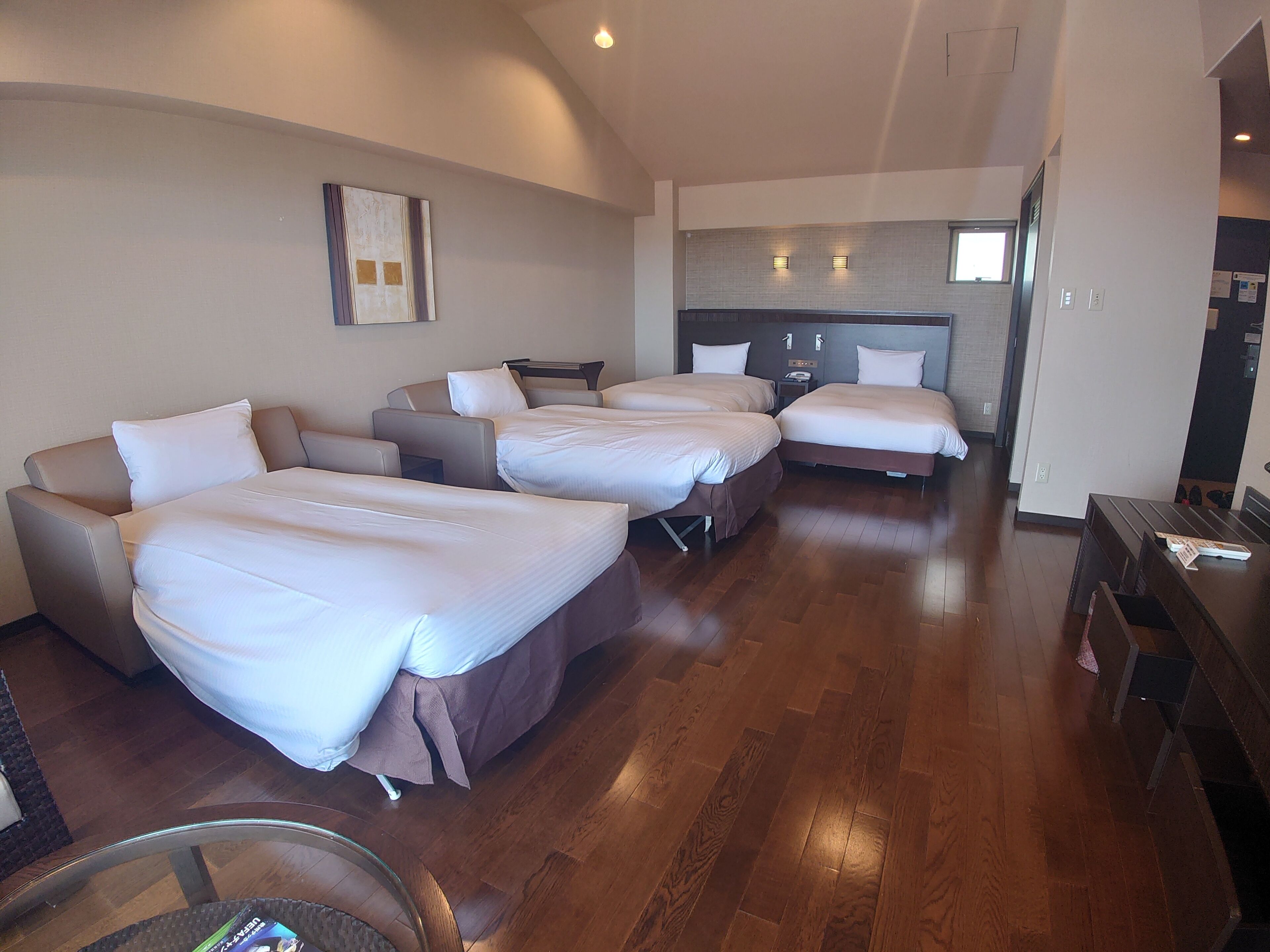 Habitación de hotel con cuatro camas dispuestas en forma de U, una kitchenette al fondo y piso de madera.