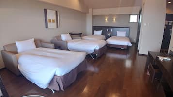Habitación de hotel con cuatro camas dispuestas en forma de U, una kitchenette al fondo y piso de madera.