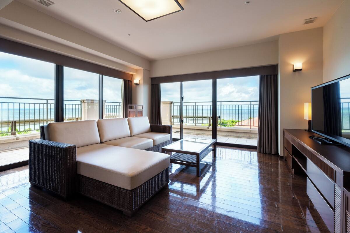 Un balcon spacieux avec un canapé et un téléviseur à écran plat, de grandes fenêtres offrant une vue sur la mer et un plancher en bois.