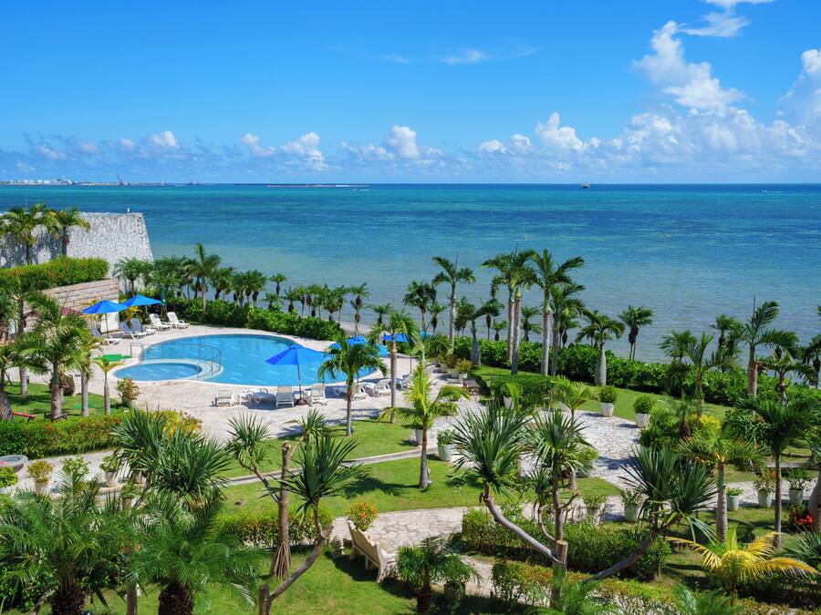A resort with a swimming pool, lounge chairs, and palm trees.