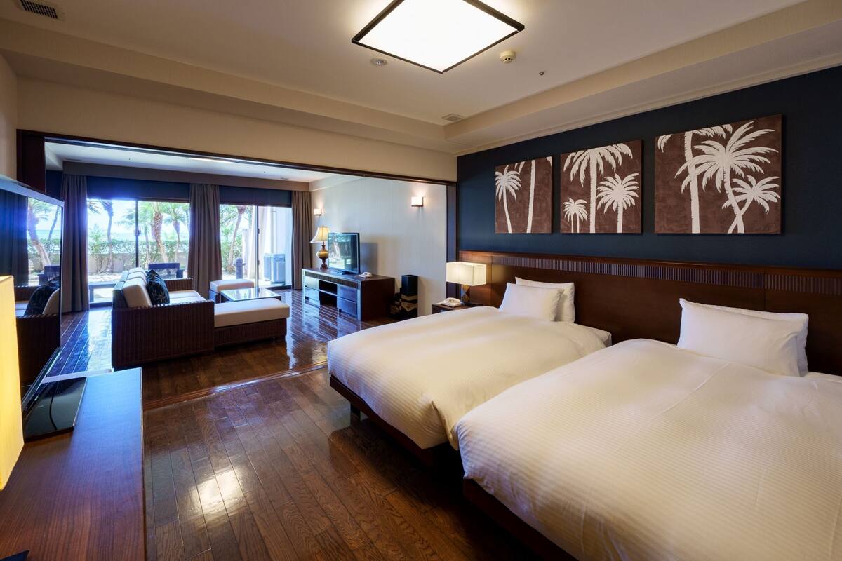 Une chambre d’hôtel avec deux lits, un bureau, une télévision et une vue sur les palmiers.