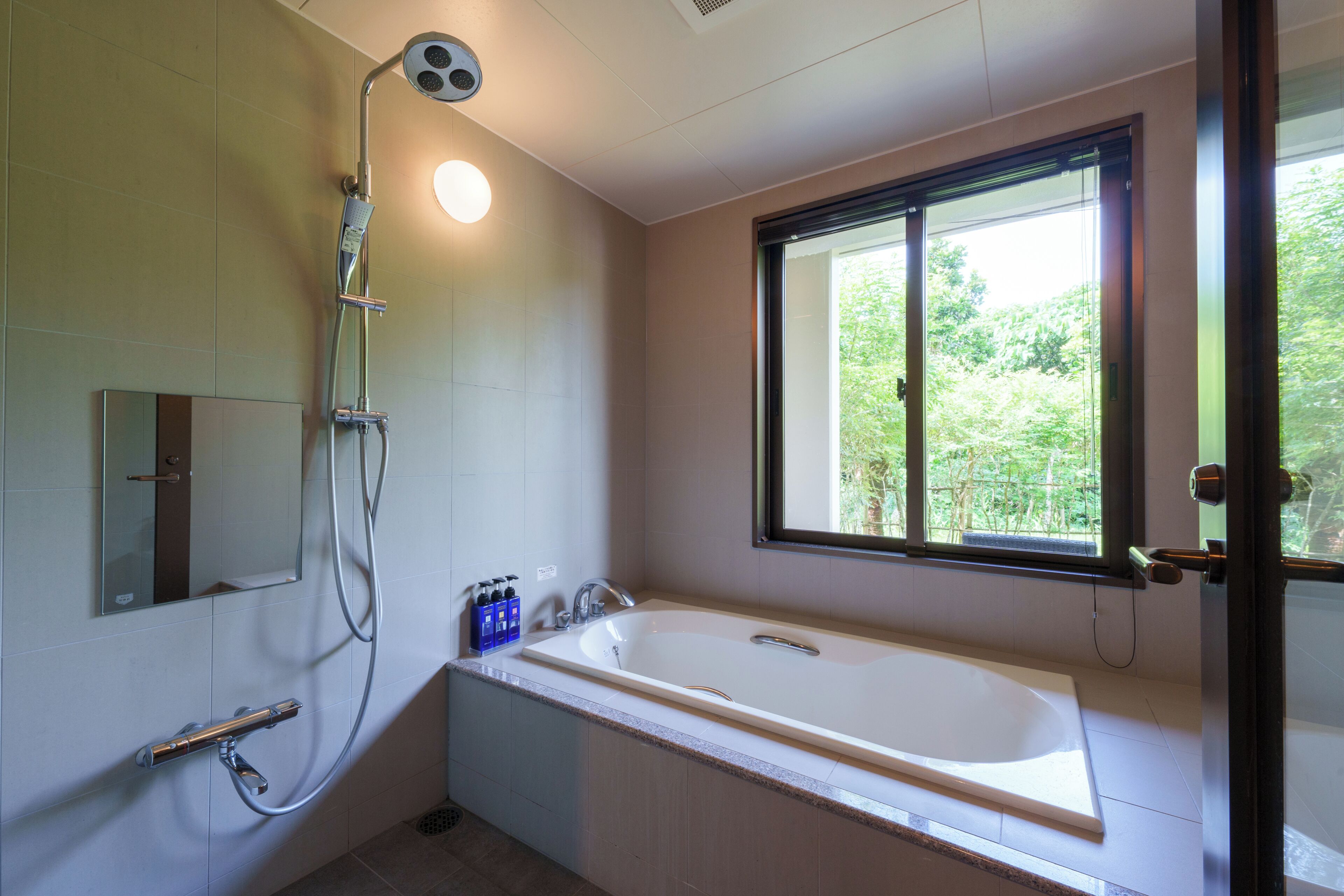 A bathroom with a bathtub, a shower, a window, and a mirror.