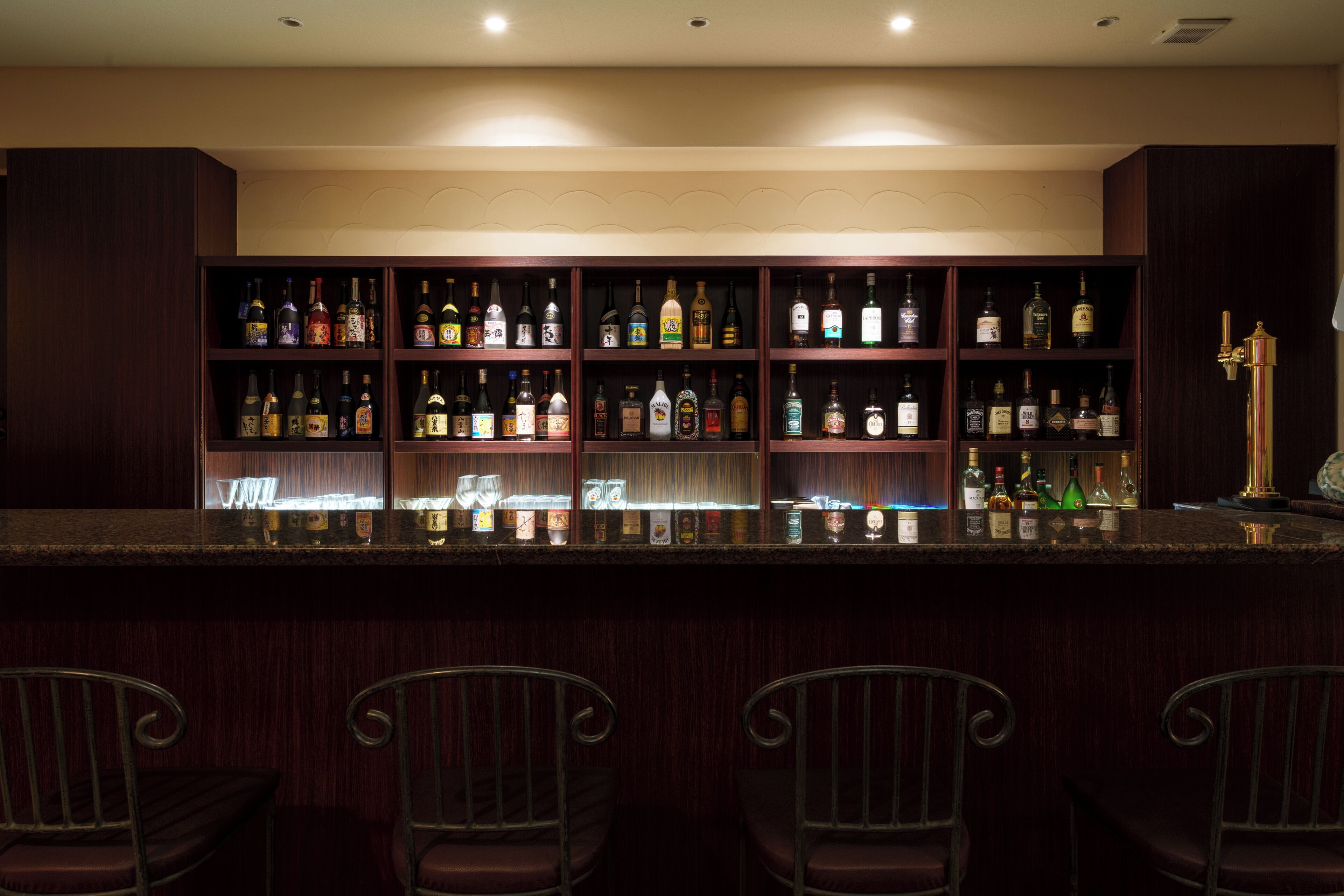A bar area with multiple shelves of liquor bottles, a marble countertop, and bar stools.