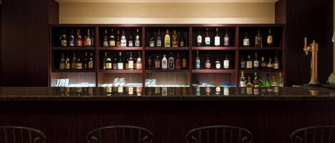 Una zona de bar con varias estanterías llenas de botellas de licores, una encimera de mármol y taburetes.