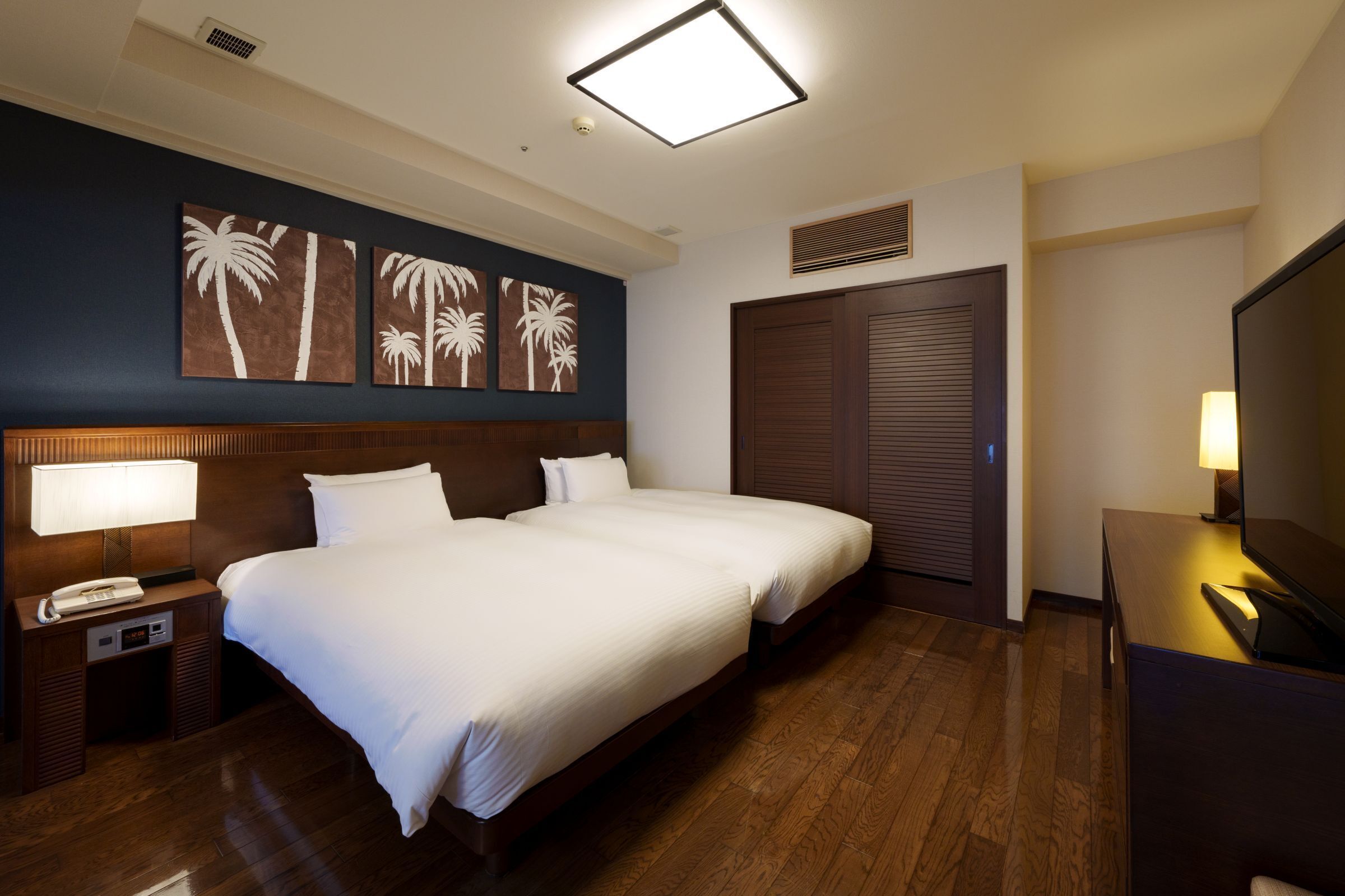 Ein Hotelzimmer mit einem großen Bett, zwei Nachttischen, einem Fernseher und Kunstwerken an der Wand.