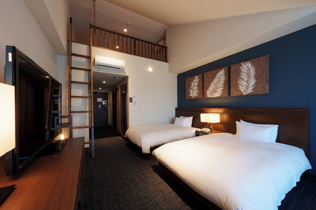 Une chambre d’hôtel avec deux lits, un bureau, une échelle et une œuvre d’art accrochée au mur.