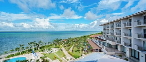 A hotel with a pool, palm trees, and a view of the ocean.